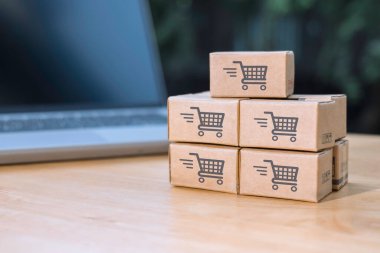 İnternetten alışveriş veya ecommerce ve dağıtım hizmeti konsepti için dizüstü bilgisayarında alışveriş kartı logosu olan kağıt kutular veya paket. İnternet üzerinden alışveriş hizmeti sunar ve internet üzerinden eve teslimat sunar.
