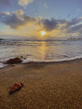 Altın gündoğumu sırasında kumlu kıyı şeridini kaplayan yumuşak dalgalar, huzur dolu okyanus manzarasını aydınlatıyor.