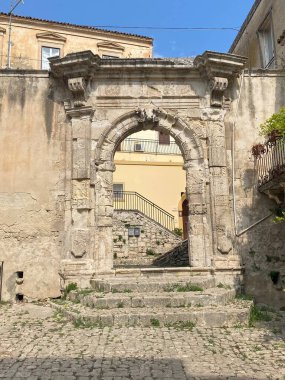 Sicilya, Modica 'daki Corso Giuseppe Garibaldi' den Salita Palermo 'ya giden tarihi kemerli Porta Palermo' nun düşük açılı görüntüsü eskimiş taş işçiliğini ve mimari detaylarını gözler önüne seriyor.