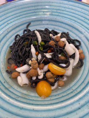 Mürekkep balıklı siyah spagetti, küçük sarı domatesler ve fregola, İtalya 'nın Giulianova kentindeki zarif bir restoranda mavi bir seramik tabakta servis ediliyor.
