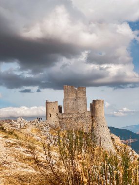 Ortaçağ Rocca Calascio kalesi kayalık tepeye tünemiş, dramatik bulutlu arazi Abruzzo dağlık arazisine bakıyor.
