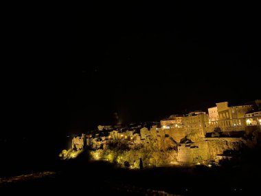 Pitigliano ortaçağ köyü volkanik kayalıklara tünemiş, gece aydınlığı altında parlıyor, büyüleyici Toskana mimari siluetlerini ortaya çıkarıyor.