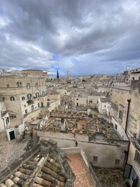 Kayalık arazide çağlayan tarihi taş konutlar, İtalya 'nın Basilicata kentindeki antik Sassi di Matera manzarasını vurgulayan dramatik bulut manzarası