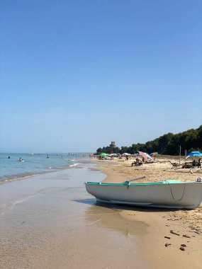 Pineto Sahili 'nin kumlu sahilindeki küçük bir teknenin manzarası. Turistler güneşli bir gökyüzünün altında Adriyatik Denizi' nin berrak mavi sularının keyfini çıkarıyorlar.
