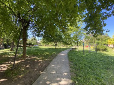 İtalya 'nın Pescara kentinin ılık güneş ışığıyla yıkanmış ağaçlar, banklar ve bir oyun parkının bulunduğu yemyeşil bir parktan geçen beton yol.