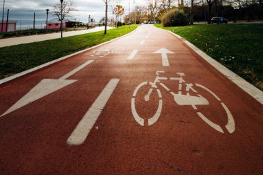 Adanmış kırmızı bisiklet yolu kentin yeşil alanından geçen beyaz yönlü oklar ve bisiklet sembolü ile işaretlenmiş.