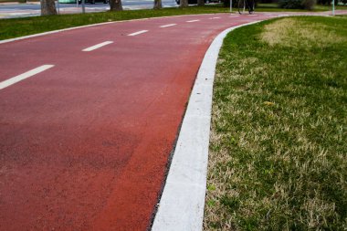 Beyaz betonla çevrili ve yemyeşil çimlerle çevrili bir parkın içinden geçen sarmal kırmızı bisiklet yolu, açık hava eğlencelerini davet ediyor.