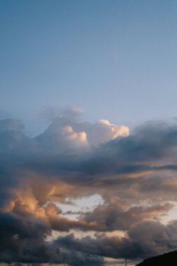 Turuncu, pembe ve gri renklerle gökyüzünü boyayan canlı günbatımı bulutları dramatik atmosfer güzelliği yayıyor.