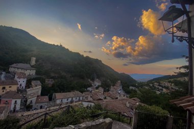 Günbatımı manzarası ortaçağ Preci köyünü aydınlatıyor, altın ışık tarihi Umbria manzarasını dramatik bulutlarla kaplıyor.
