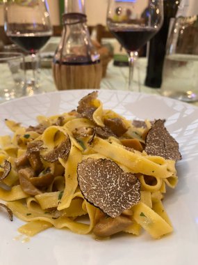 Tagliatelle makarnası yer mantarı dilimleri ve mantarlarla süslenir, bir Toskana restoranında beyaz bir tabakta servis edilir, yanında da kırmızı şarap.