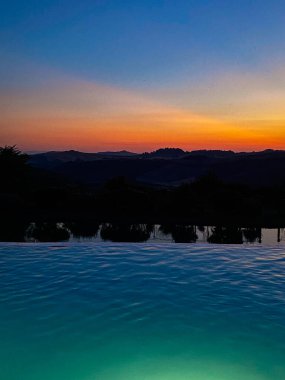 Renkli günbatımı Toskana kırsalındaki sakin bir yüzme havuzunun sakin sularını yansıtarak huzurlu ve rahatlatıcı bir atmosfer yaratıyor.