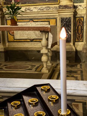 Ön planda tek bir elektrikli adak mumu parlak bir şekilde yanar. Süslü sunakta ve Tuscany, Barberino Tavarnelle 'deki bir kilisede mermer üzerine yumuşak bir parıltı yayar.