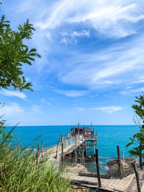 Geleneksel ahşap balıkçı iskelesi turkuaz suları boyunca uzanır, mavi bulutlu gökyüzü tarafından çerçevelenir Rocca San Giovanni, Abruzzo kıyı şeridi yakınlarında