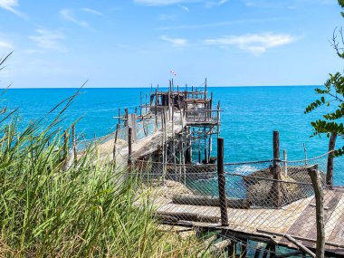 Rocca San Giovanni yakınlarındaki turkuaz Adriyatik suları üzerinde uzanan ahşap iskele, İtalya 'nın kıyı manzarası güneş ışığında banyo yapıyor.