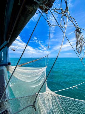 Adriyatik kıyısındaki geleneksel bir balıkçı teknesinde asılı duran balıkçı ağı mavi deniz ve gökyüzü manzarası sunuyor.