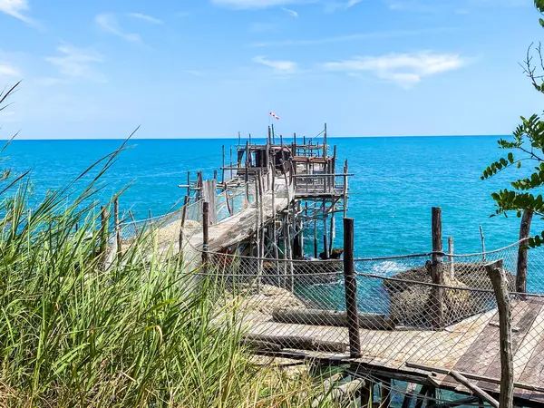 Rocca San Giovanni yakınlarındaki turkuaz Adriyatik suları üzerinde uzanan ahşap iskele, İtalya 'nın kıyı manzarası güneş ışığında banyo yapıyor.