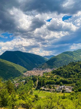 İtalya 'nın Abruzzo bölgesinde büyüleyici bir köy olan Scanno' nun panoramik manzarası, dramatik bulutlu bir gökyüzünün altında yemyeşil dağların arasına yerleşmiştir.