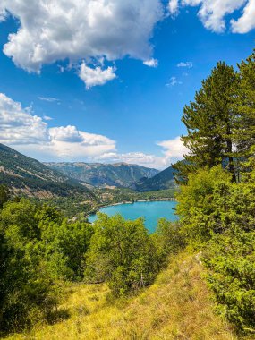 İtalya 'nın Abruzzo kentindeki tüylü bulutlu mavi gökyüzü altında gür bitki örtüsü ve dağlarla çevrili göz alıcı bir manzara.