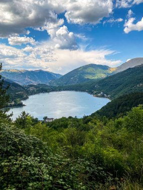 Scanno Gölü 'nün nefes kesici manzarası bulutlu gökyüzünü yansıtıyor, İtalya' nın Abruzzo kentindeki yemyeşil dağların arasına yerleşmiş, sakin ve pitoresk bir manzara yaratıyor.