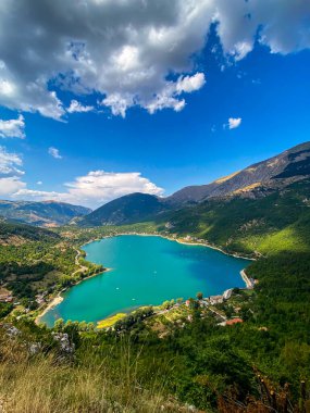 Scanno Gölü, kısmen bulutlu bir gökyüzü altında, yemyeşil yemyeşil ve İtalya 'nın görkemli dağlarıyla parlar.
