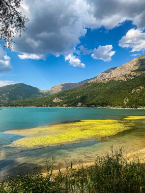 Sarı su bitkileriyle Scanno Gölü 'nün nefes kesici manzarası bulutlu gökyüzünü ve İtalya' nın Abruzzo kentindeki dağları yansıtıyor.
