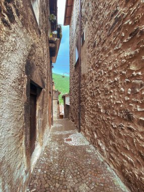 İtalya, Abruzzo, Scanno 'da dar bir kaldırım taşından geçitten geçen taş evler yeşil tepeleri ve mavi gökyüzünü bir an için yokuş yukarı götürüyorlar.
