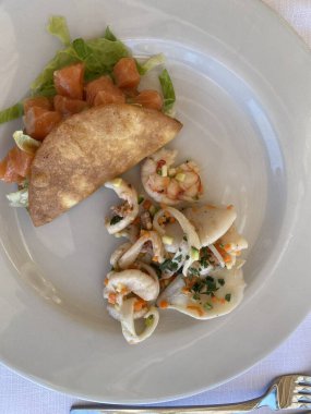 Kalamar ve karidesli deniz ürünleri salatası, yanında canlı bir somon taco ve taze marul, popüler bir İtalyan aperatifi oluşturuyor.