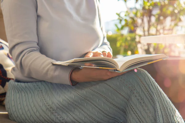 Woman near the window in a knitted sweater holding and reading a book. Relaxation concept. Close up