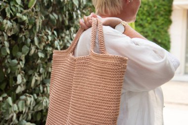 Woman holds a handmade beige knitted bag in her hand outdoors. Sustainable shopping. Wasteless lifestyle. Female with a jute bag with her own hands on a walk