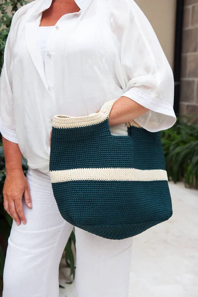 Woman holds a handmade blue knitted bag in her hand outdoors. Sustainable shopping. Wasteless lifestyle. Female with a jute bag with her own hands on a walk