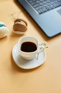 Düz uzanış, üst düzey ofis masası, dizüstü bilgisayarlı çalışma alanı, kahve fincanı ve çiçekli badem kurabiyesi, turuncu arka planda, evden çalışma, uzak çalışma