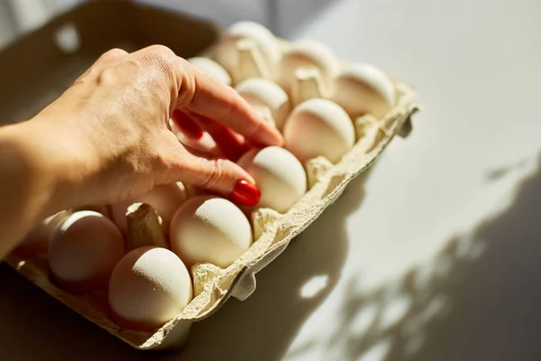 Woman hand take egg from cardboard box eggs on white background, hard sunlight, Organic egg pack product.
