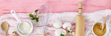 Banner Pastanesi ya da içinde çiçekler, malzemeler, pembe arka planda hamur işi için mutfak malzemeleri, bahar pişirme teması. Üst görünüm, alanı kopyala.