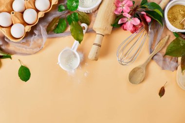 Çiçekli fırın ya da yemek çerçevesi, malzemeler, pastel turuncu arka planda hamur işi için mutfak malzemeleri, bahar pişirme teması. Üst görünüm, alanı kopyala.