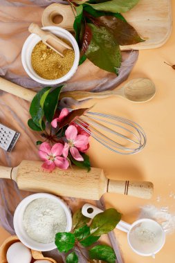 Bakery  or cooking frame with flower, ingredients, kitchen items for pastry on pastel orange background,  spring cooking theme. Top view, copy space.