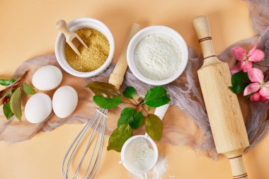 Bakery  or cooking frame with flower, ingredients, kitchen items for pastry on pastel orange background,  spring cooking theme. Top view, copy space.