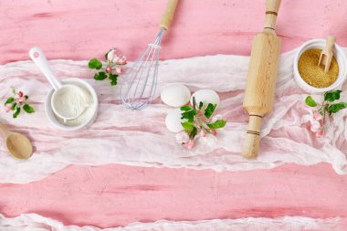 Çiçekli fırın veya yemek iskeleti, malzemeler, pembe arka planda hamur işi için mutfak malzemeleri, bahar pişirme teması. Üst görünüm, alanı kopyala.