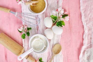 Çiçekli fırın veya yemek iskeleti, malzemeler, pembe arka planda hamur işi için mutfak malzemeleri, bahar pişirme teması. Üst görünüm, alanı kopyala.