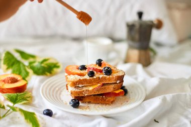 Breakfast on white bed sheets, good morning, summer french toast with cream cheese, honey, peaches and blueberries, coffee, flowers, Hotel room early morning, honeymoon