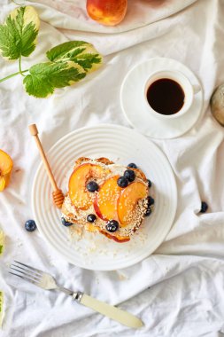 Top view Breakfast on white bed sheets, good morning, summer french toast with cream cheese, honey, peaches and blueberries, coffee, flowers, Hotel room early morning, honeymoon