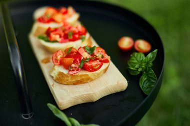 İtalyan bruschetta 'sı taze kırmızı domatesler ve fesleğenli otlar bahçedeki ahşap tahta üzerinde, arka bahçede, evde, gün ışığında. Klasik İtalyan yemeği, antipasto.
