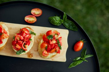 İtalyan bruschetta 'sı taze kırmızı domatesler ve fesleğenli otlar bahçedeki ahşap tahta üzerinde, arka bahçede, evde, gün ışığında. Klasik İtalyan yemeği, antipasto.