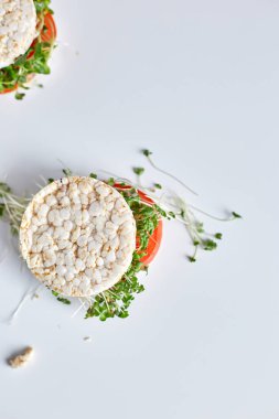 Üst Manzara Sağlıklı burger Çıtır pirinç ekmeği sebzeli domates ve beyaz arka planda mikro yeşiller, vegan beslenme, diyet yemekleri