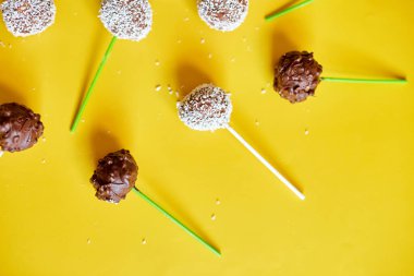 Flat lay delicious homemade popcake coconut and dark chocolate cake pops on a yellow background, festival desserts, tasty food