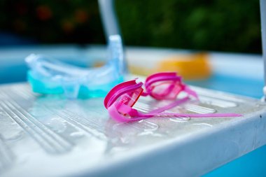 Yüzen pembe gözlükler, mavi dalış maskesi dışarıdaki havuz basamaklarında yatıyor, yaz tatili..