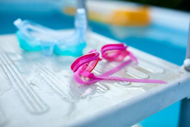 Yüzen pembe gözlükler, mavi dalış maskesi dışarıdaki havuz basamaklarında yatıyor, yaz tatili..