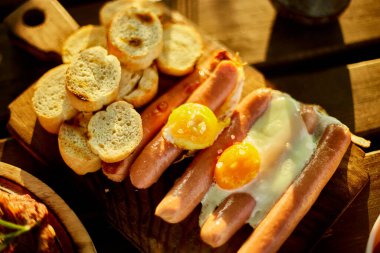 Kırsal bir ahşap tahtada sunulan sahanda yumurta ve sosislerin yer aldığı samimi geleneksel bir İngiliz kahvaltısının yakın çekimi klasik bir sabah yemeğini vurguluyor..