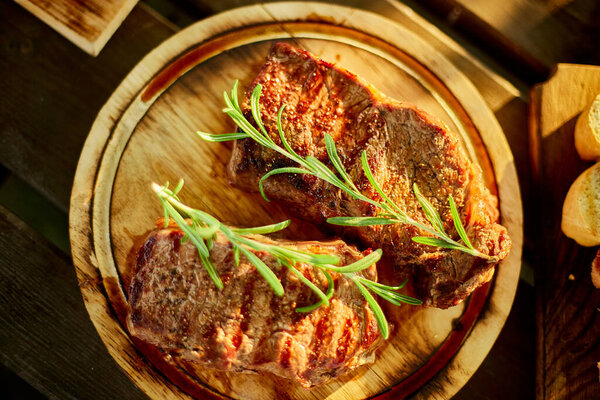 A succulent ribeye steak, perfectly grilled and adorned with fresh rosemary sprigs, rests on a circular wooden plate against a dark, rustic backdrop.