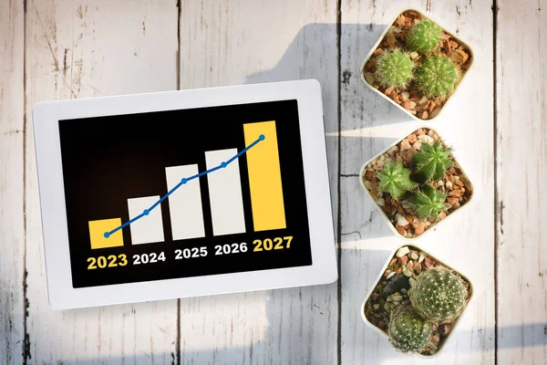 Green technology business with five years forecast on computer tablet with cactus on desk background. Clean energy to sustainable future concept and alternative energy idea