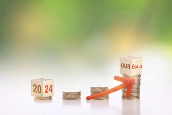 New year 2024 to our goal written on cube on stack of coins on abstract background. Saving with return on investment concept and sustainable economic growth idea